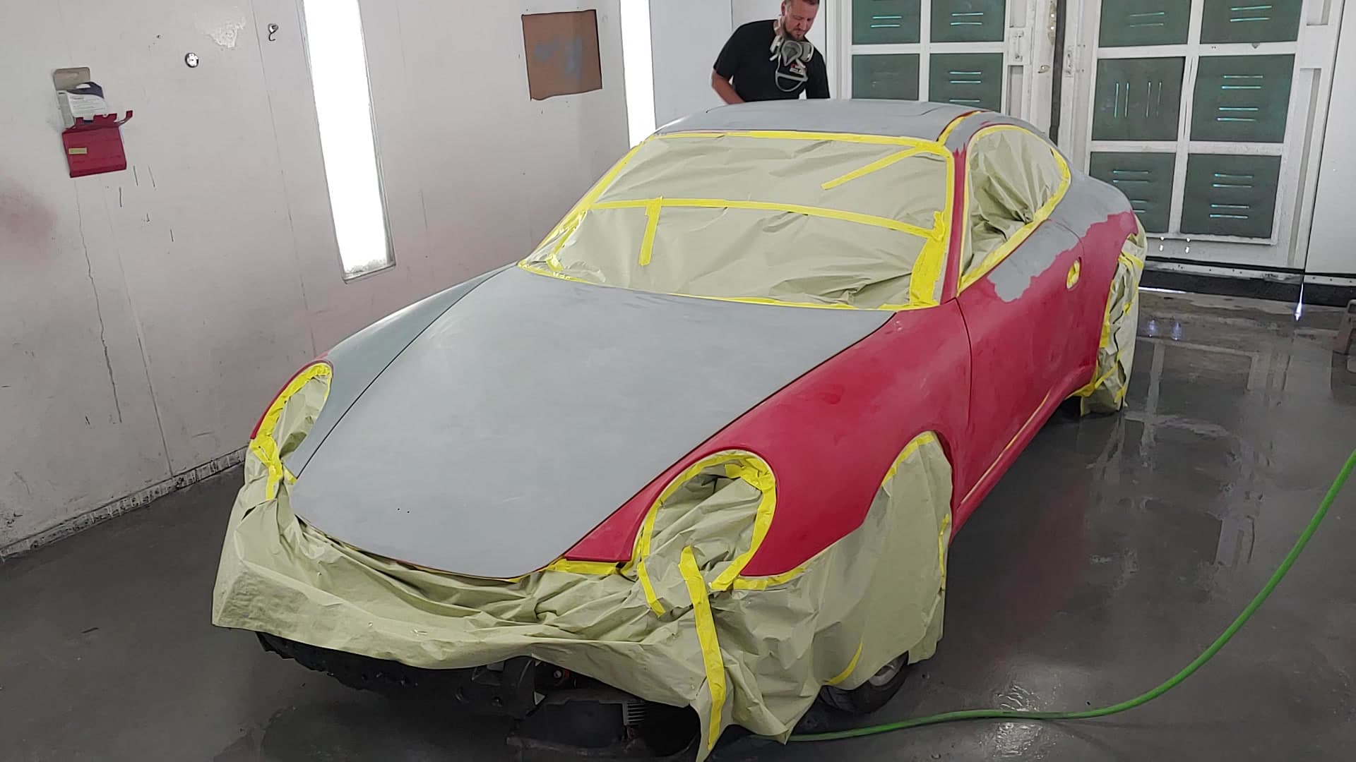 A car masked in tape and film mid-repaint inside the D&D Auto Body spray booth