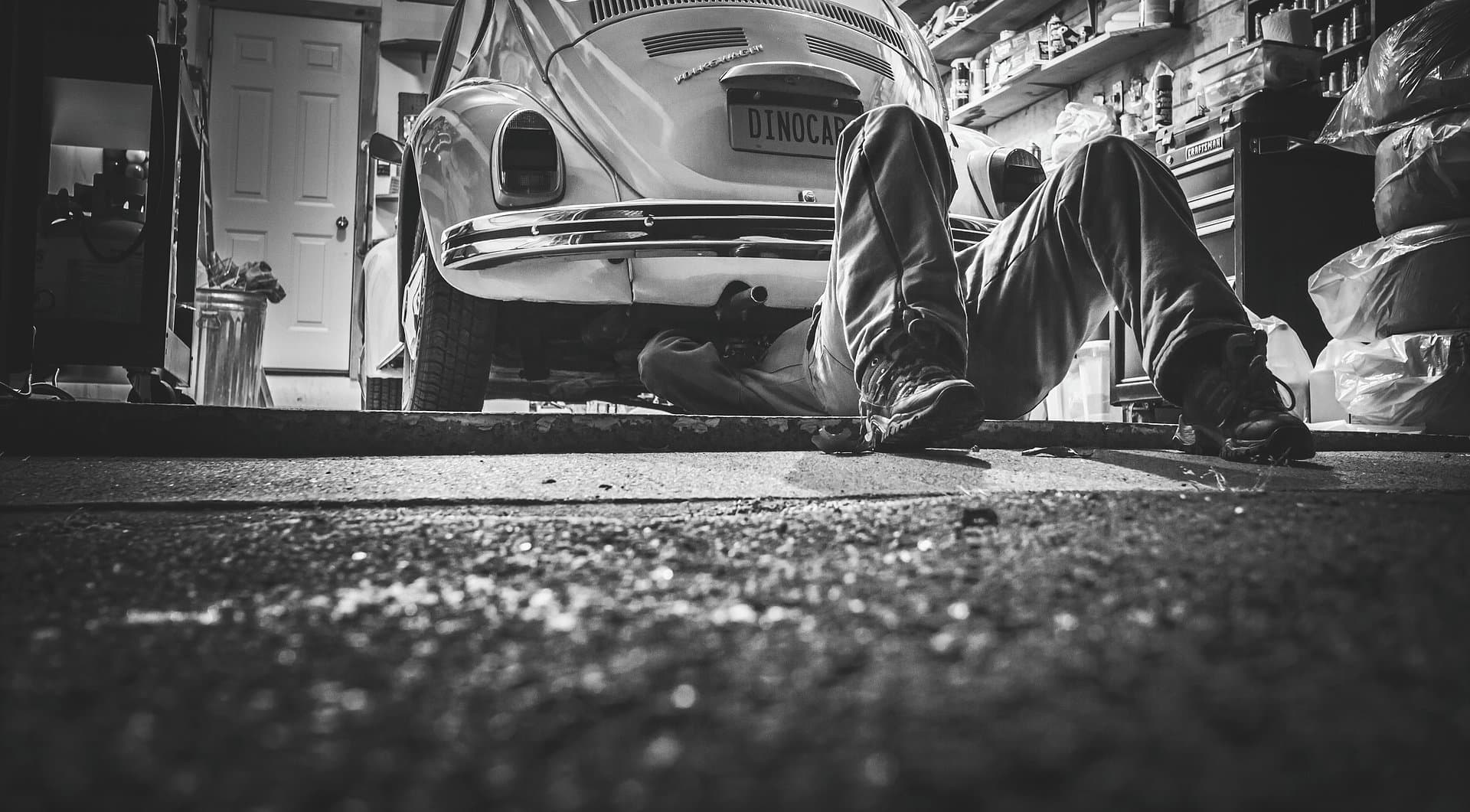 Black and white photo of a mechanic working underneath a classic car at D&D Auto Body